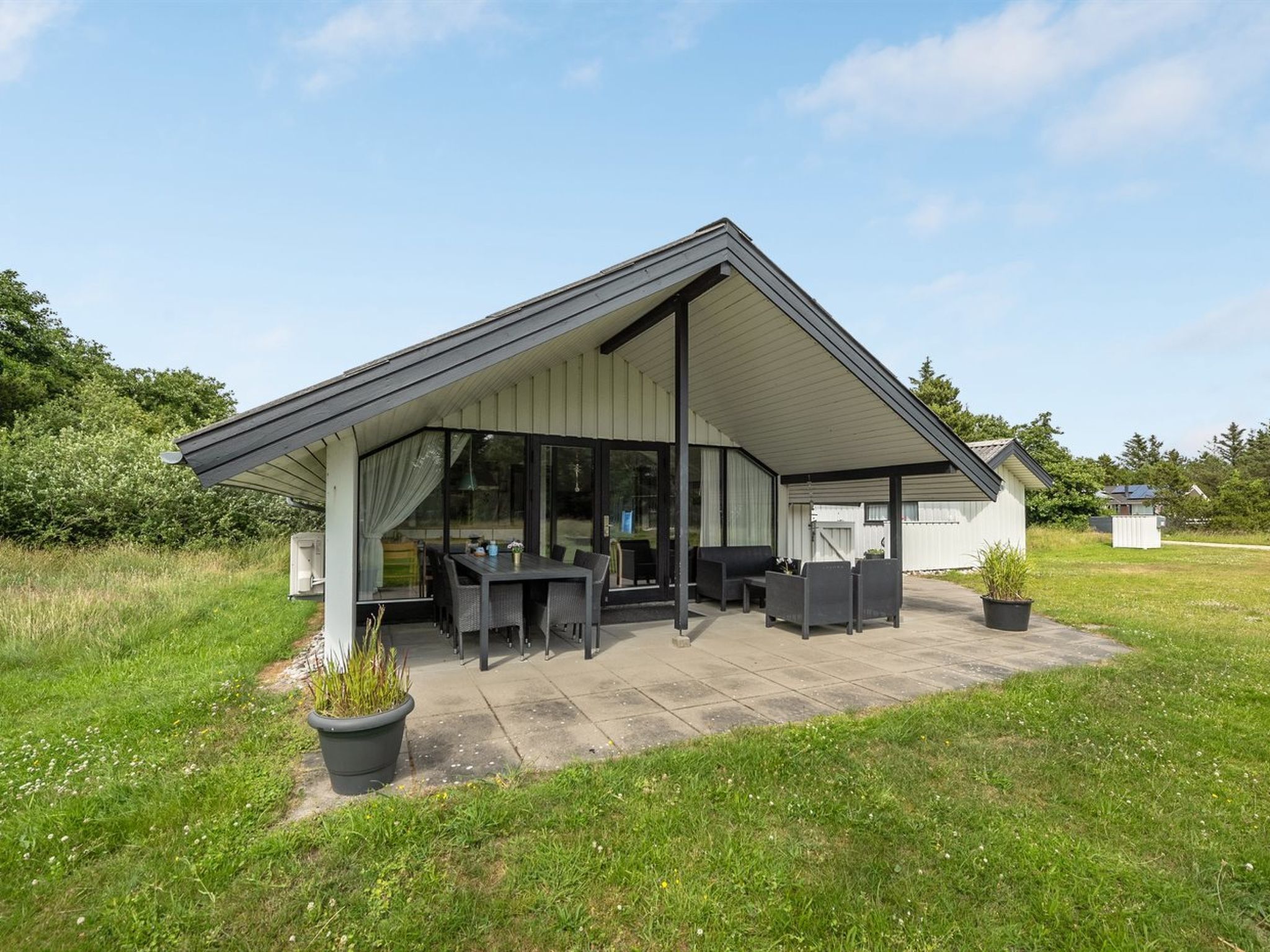Een modern huis met een overdekte patio, buitenmeubels en een groot raam met uitzicht op een grasveld.
