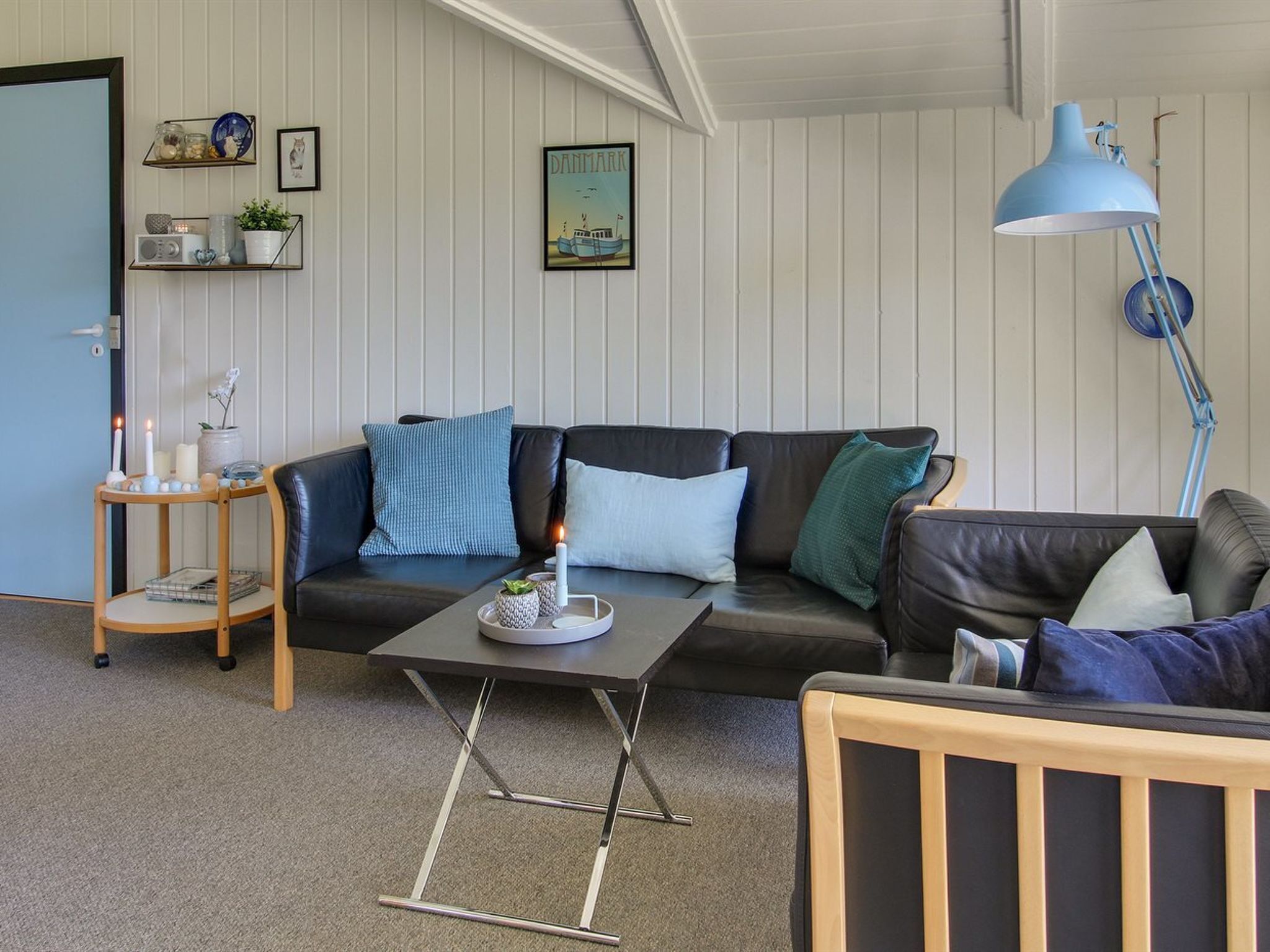 A cozy living room with a dark leather sofa, a wooden coffee table, and a blue floor lamp.