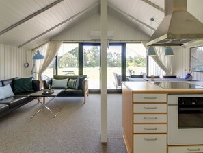 Een moderne, open woon- en eetruimte met een hoge plafond, grote ramen en een kitchenette.