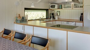 Cocina compacta con una isla central, un fregadero y un microondas. Hay sillas de madera y una mesa con mantel estampado.