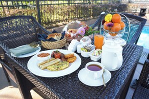 A table set with breakfast items including eggs, sausages, and toast, alongside a fruit bowl and a pitcher of orange juice.