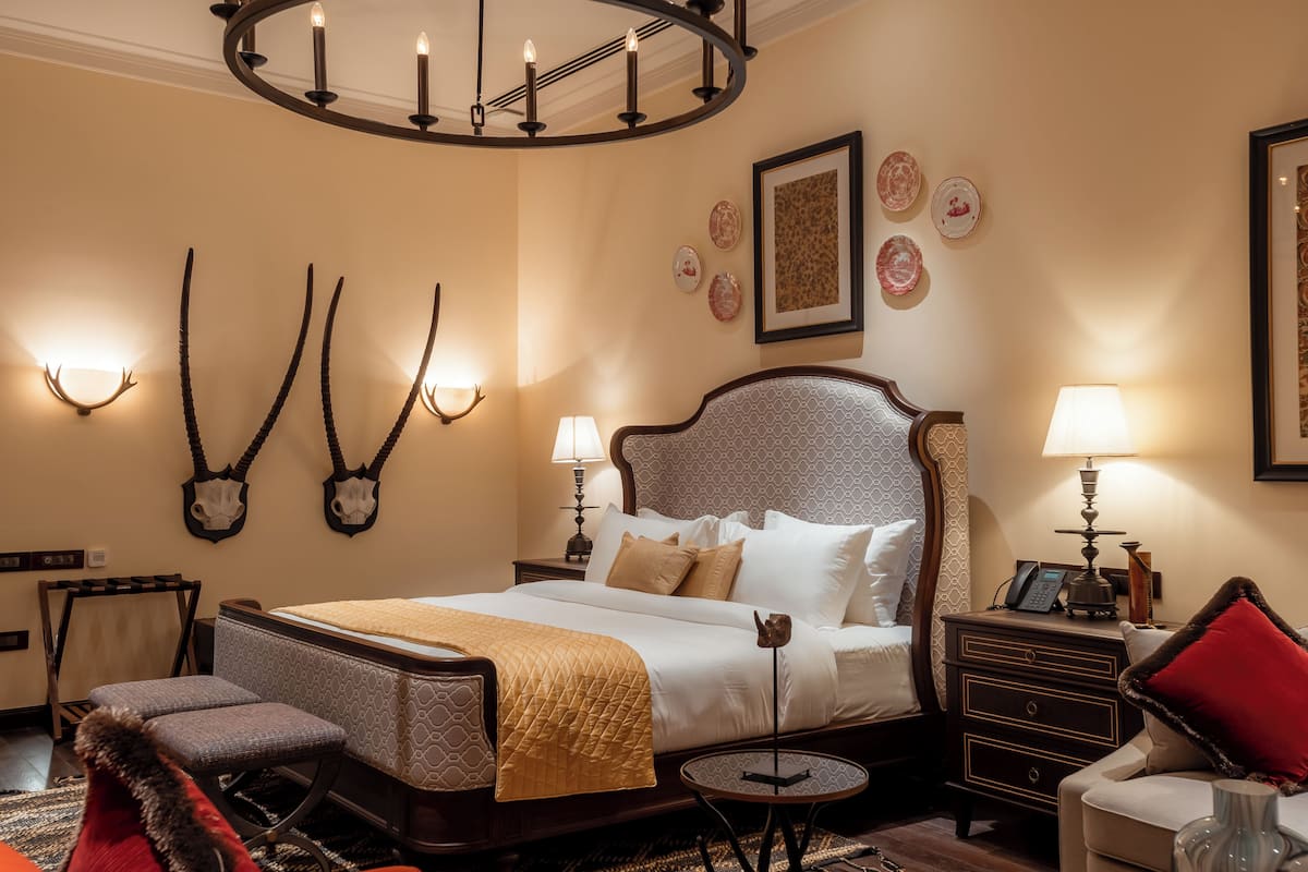 Une chambre d’hôtel avec un grand lit, des tables de chevet, une chaise, une petite table et un lustre.