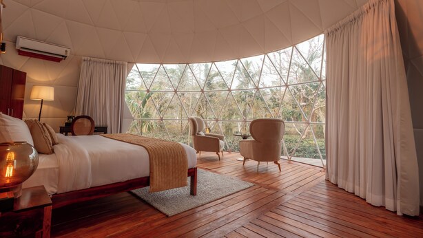 Un dormitorio con una cama grande, piso de madera, una ventana con cortinas y vistas a árboles.
