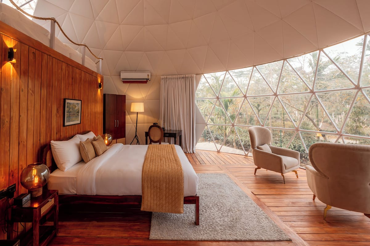 Une chambre spacieuse avec un grand lit, des murs en bois, une vue à travers une fenêtre aux formes géométriques et un coin salon confortable.