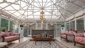 Un invernadero con techo de vidrio, muebles ornamentales y una mesa central con objetos decorativos.