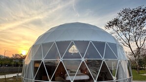 Estructura en forma de domo geodésico con una cubierta de madera y una cama en su interior.