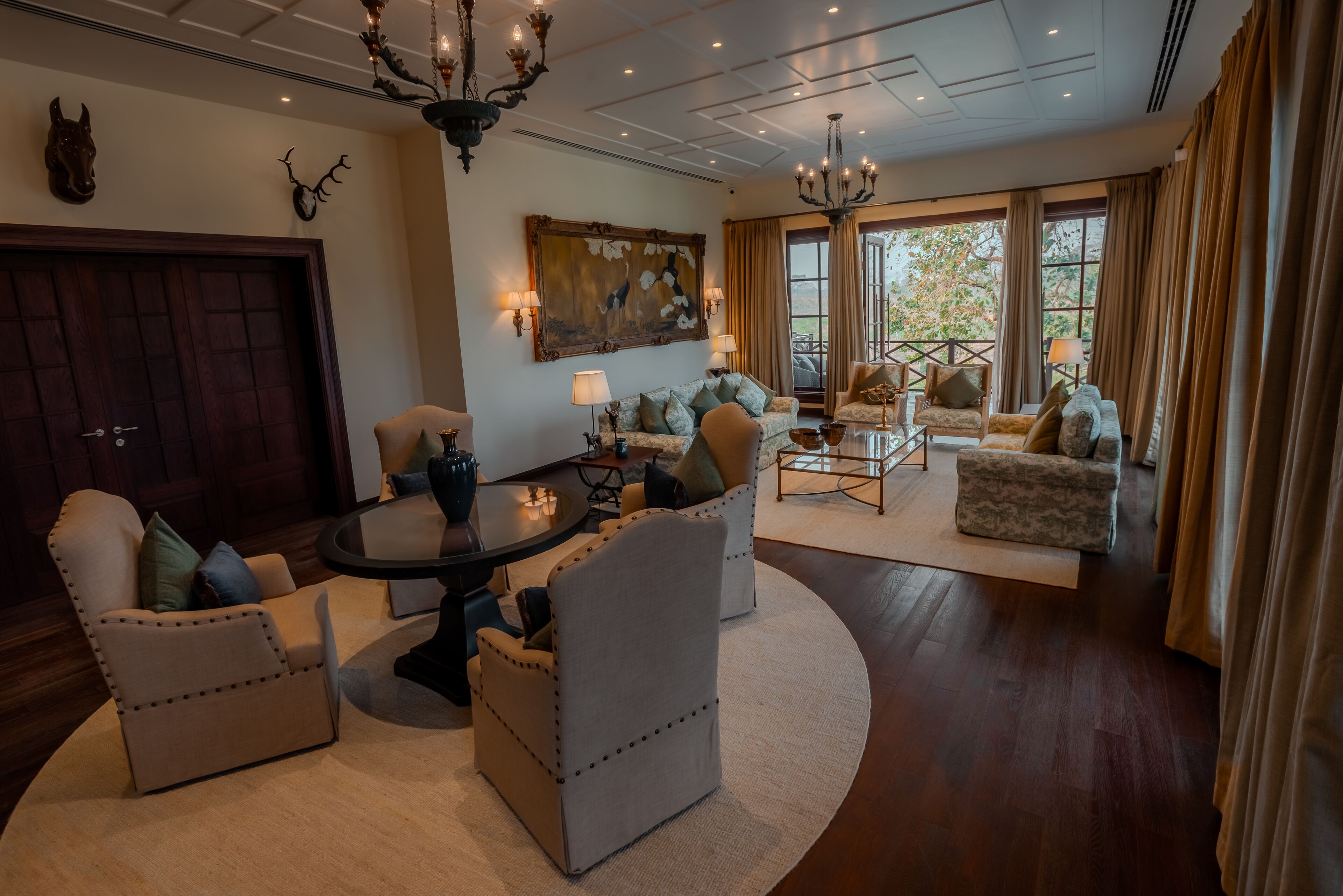 A spacious living room with a round coffee table, two armchairs, a sofa, and a chandelier.
