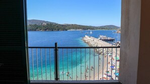 Un balcón con vista a una playa, barcos y una colina distante.
