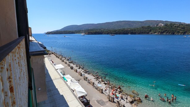 Vista costera con playa, agua cristalina y montañas al fondo.