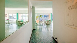 Un pasillo de hotel con vistas a un balcón, un área de comedor con sillas y una mesa, y un gran dibujo arquitectónico enmarcado en la pared.