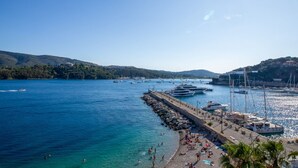 Una marina costera con barcos, una playa de arena y un rompeolas rocoso.