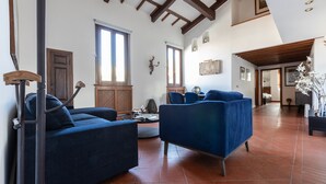 A spacious living area with a high ceiling, large windows, and a wooden ceiling beam. There are two blue sofas and a round coffee table. - Italianway - Bigli 6 (Milan)