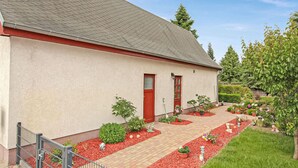 A building with a red door and windows, surrounded by a garden with various plants and a brick pathway. - 2 bedroom cozy home in Eggesin (Eggesin)