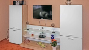 A modern living room with a flat-screen TV mounted on the wall, a glass coffee table, and a wooden cabinet with a built-in TV stand. - 2 bedroom cozy home in Eggesin (Eggesin)