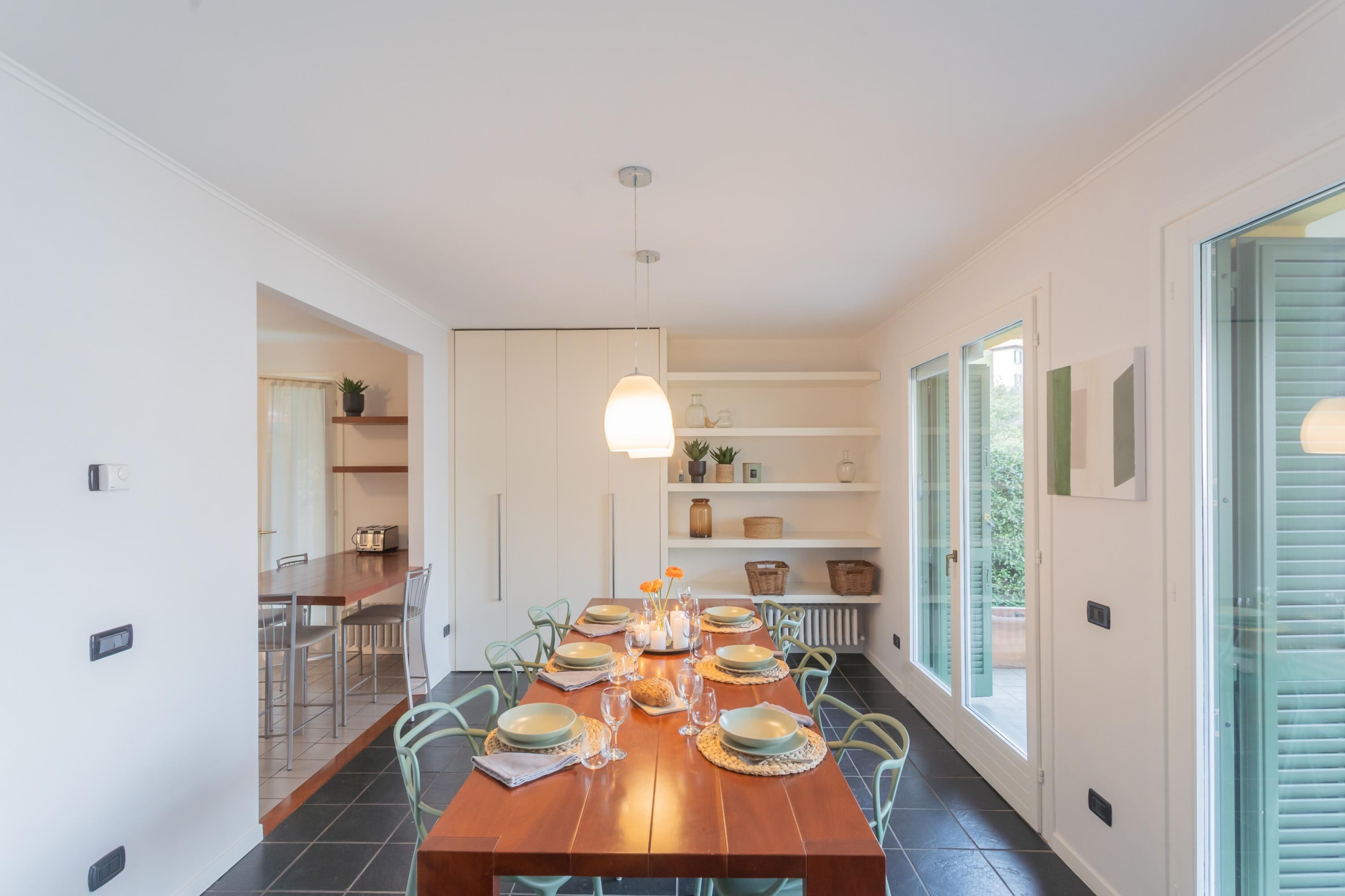 Comedor con mesa de madera dispuesta para seis personas, rodeada de sillas, con una lámpara colgante arriba.