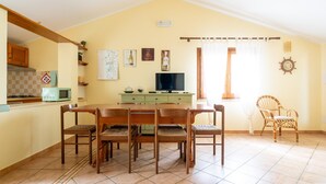 A dining area with a wooden table and chairs, a television, and a kitchen in the background. - Sa Pedrera in Sa Rocca Tunda (San Vero Milis)