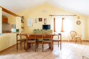 Un comedor con mesa y sillas de madera, un televisor y una cocina al fondo.