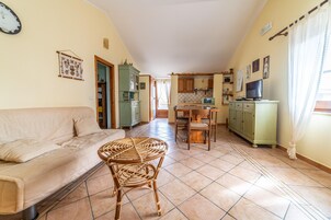 Una sala de estar con un sofá, una mesa redonda de mimbre y una cocina al fondo.