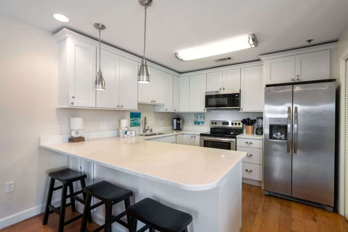 A modern kitchen with white cabinets, stainless steel appliances, and a central island with stools.