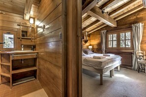 A wooden cabin interior with a wooden bed, a bathroom with a sink and shelves, and a window with curtains. - Chalet 155sqm | 360View | Quiet | Bus & Train 150m (Chamonix-Mont-Blanc)