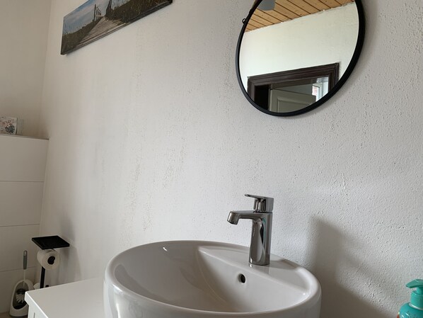 A bathroom with a white sink, a round mirror, and a picture on the wall.