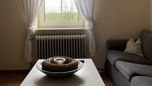 Une pièce avec une table blanche, un canapé gris et une fenêtre ornée de rideaux blancs.