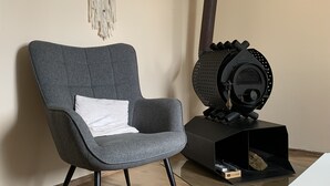 Une pièce moderne avec un fauteuil à revêtement gris, un poêle à bois noir et une décoration murale en macramé.