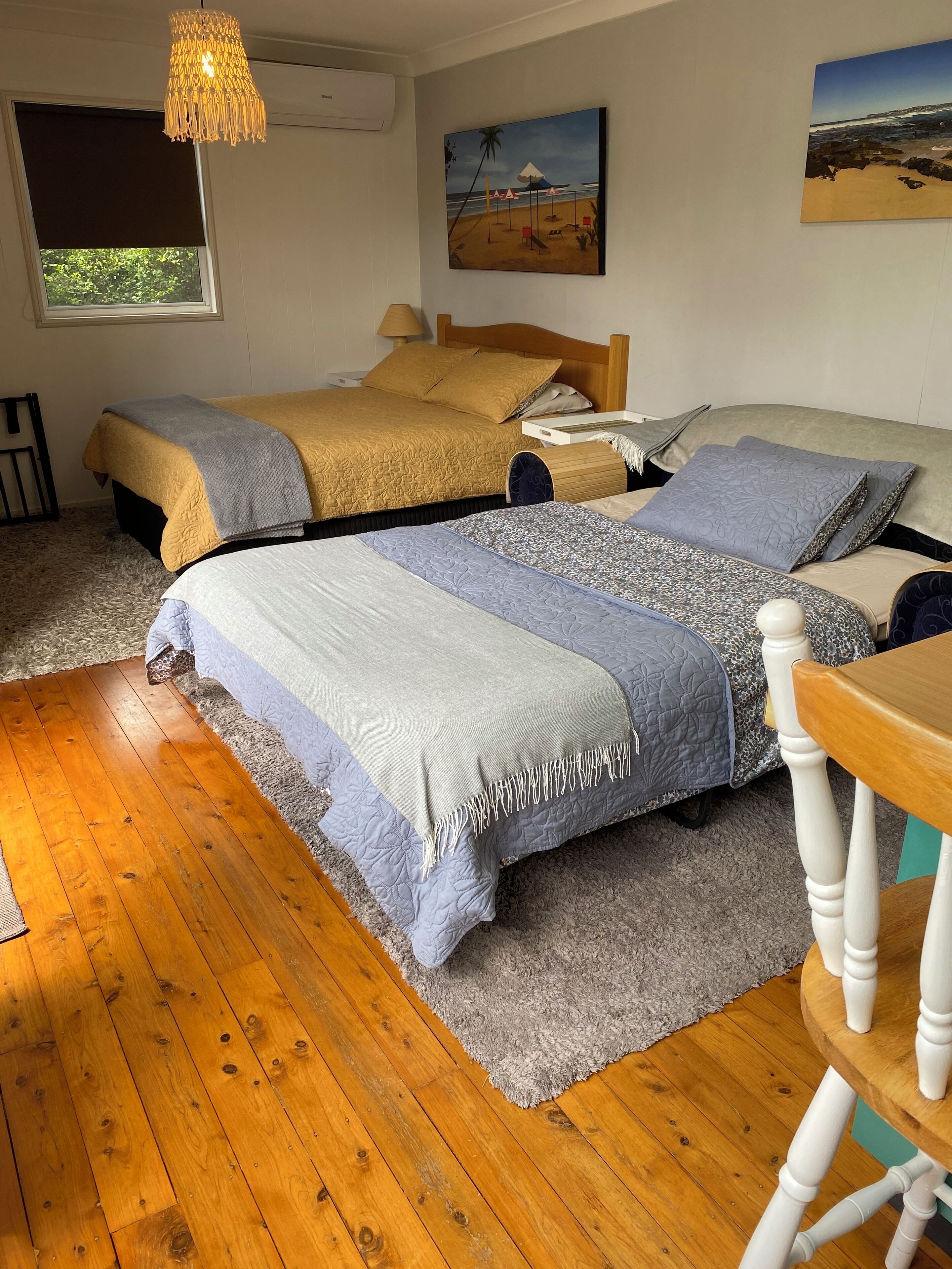 Un dormitorio con dos camas, piso de madera, una ventana y un cuadro con una playa.