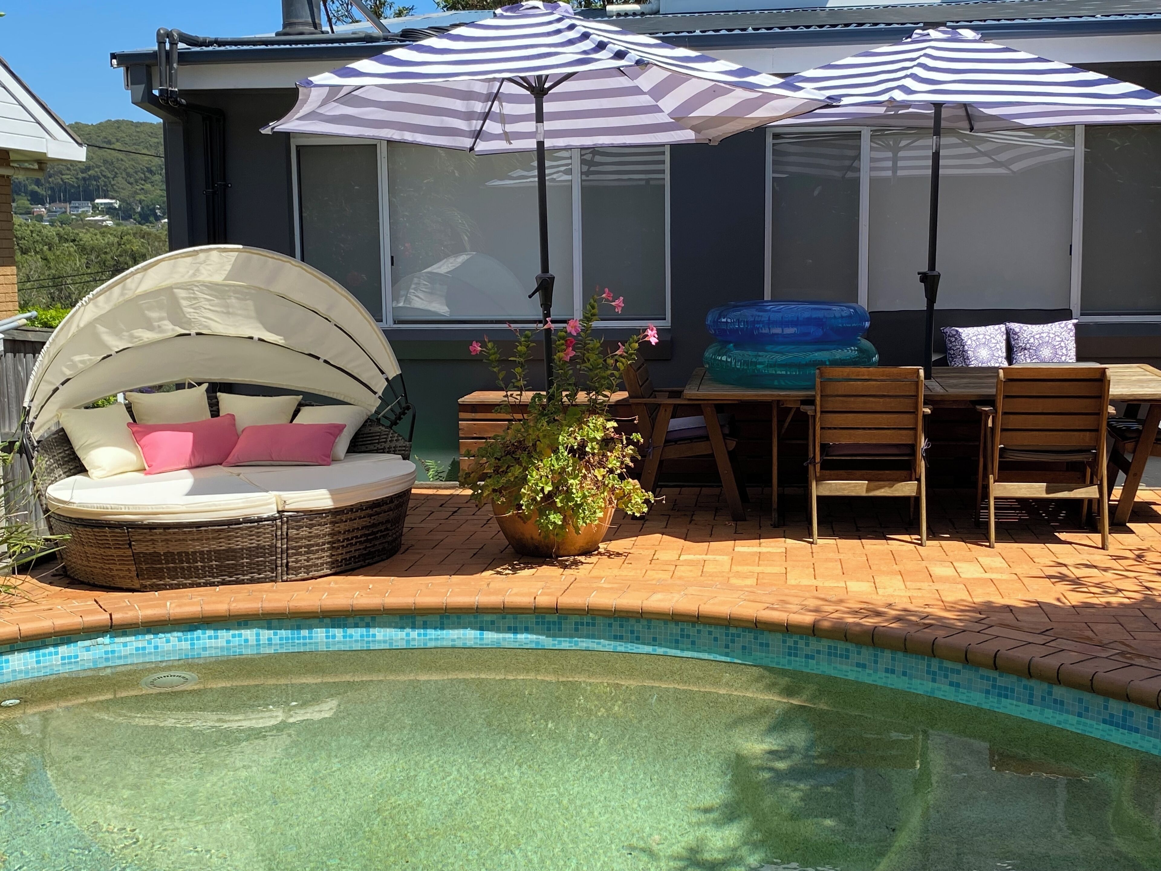 Zona junto a la piscina con una silla de mimbre, una mesa de comedor con sillas y un porche cubierto.