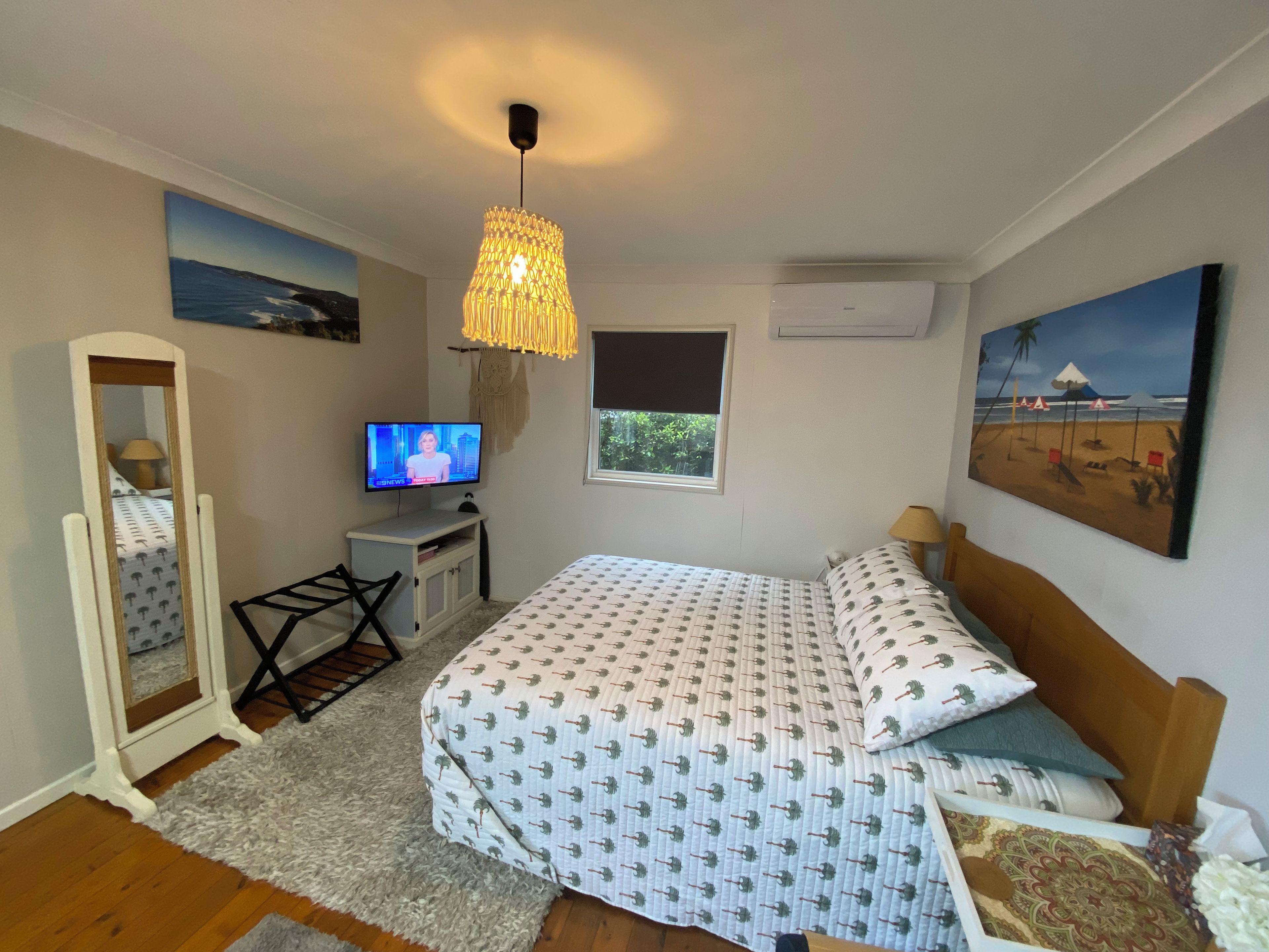 Une chambre à coucher avec un lit, une télévision, un miroir, une fenêtre et des œuvres d’art accrochées aux murs.