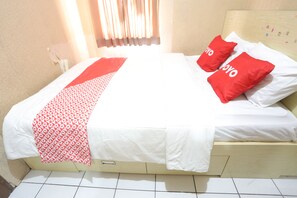 A bed with white bedding and two red pillows, a red and white patterned throw, and a wooden headboard with a number display.