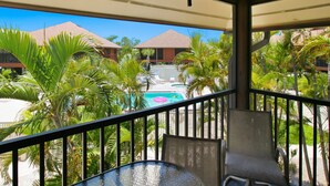 A balcony with a view of a pool, palm trees, and resort buildings. - Pet friendly paradise on Sanibel Island with private beach - Signal Inn 12 (Sanibel)