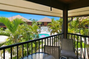 En balkon med udsigt over en pool, palmer og resortbygninger.