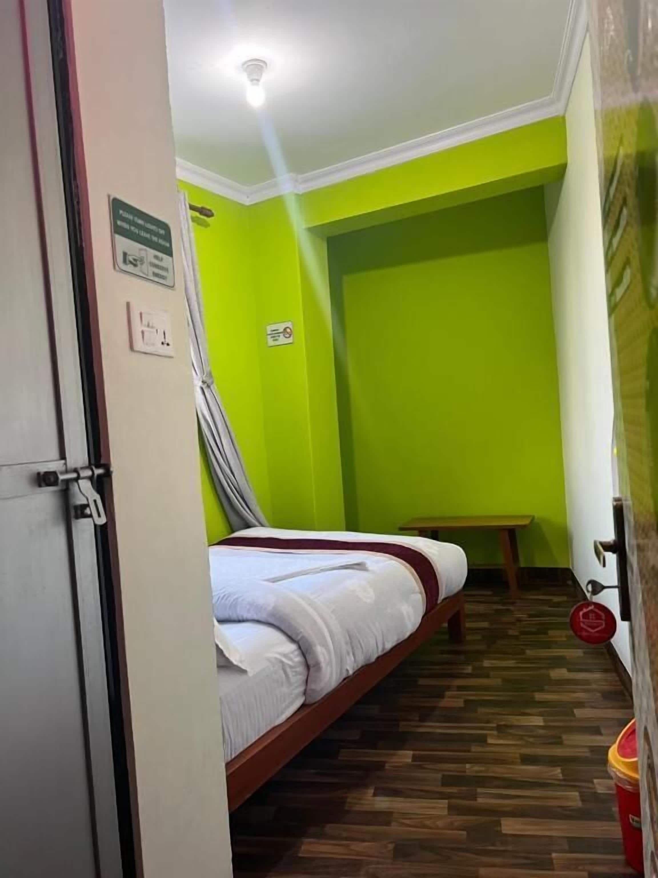A narrow room with a bed, a bench, and a trash bin.