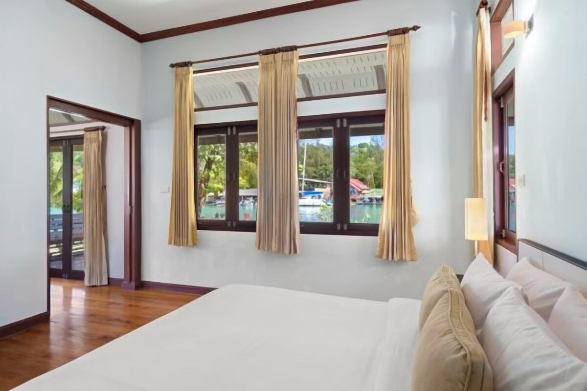 Camera d'albergo con un letto grande, tende, una finestra vista piscina e una porta che dà su un'altra zona.