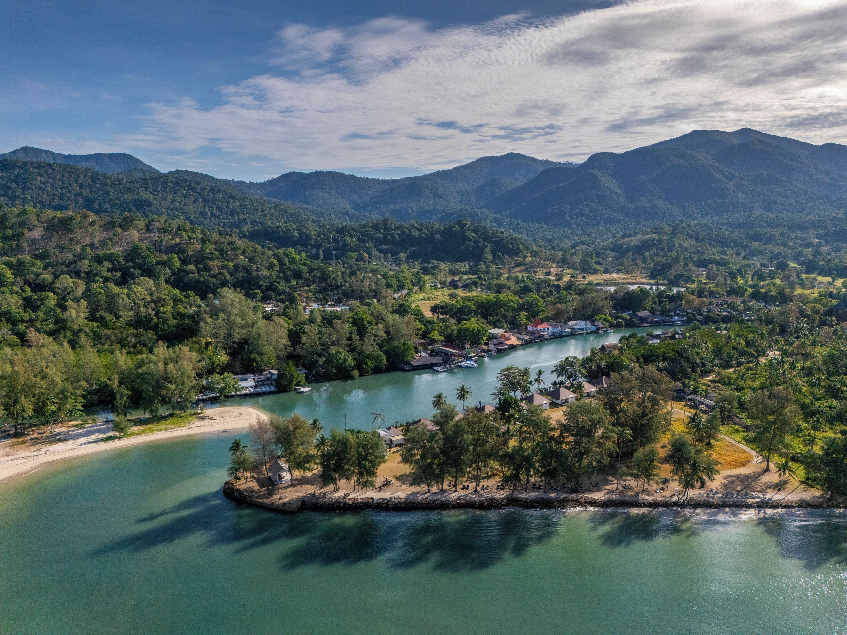 A coastal town with a river, surrounded by mountains and dense forests.