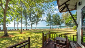 Une terrasse en bois avec une table et des chaises, donnant sur une plage bordée de palmiers et sous un ciel dégagé.