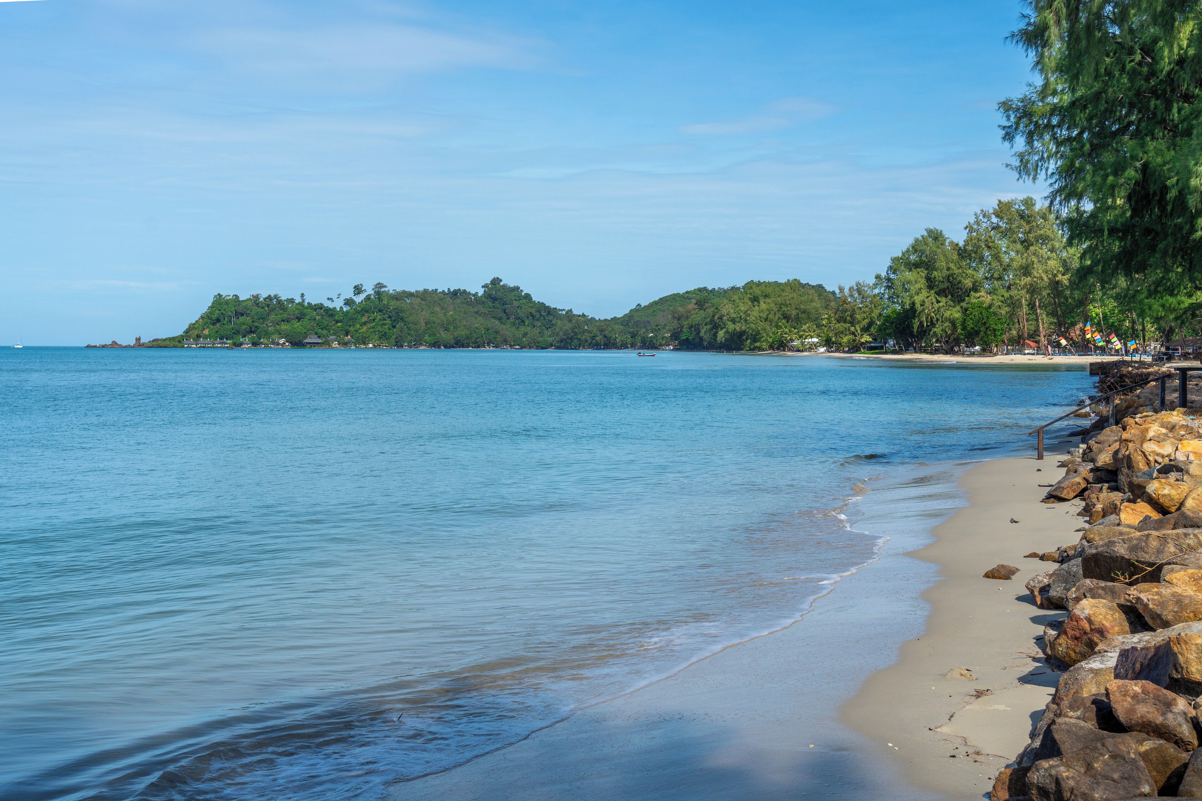 Una playa con aguas azul turquesa, costa rocosa y una isla boscosa al fondo.