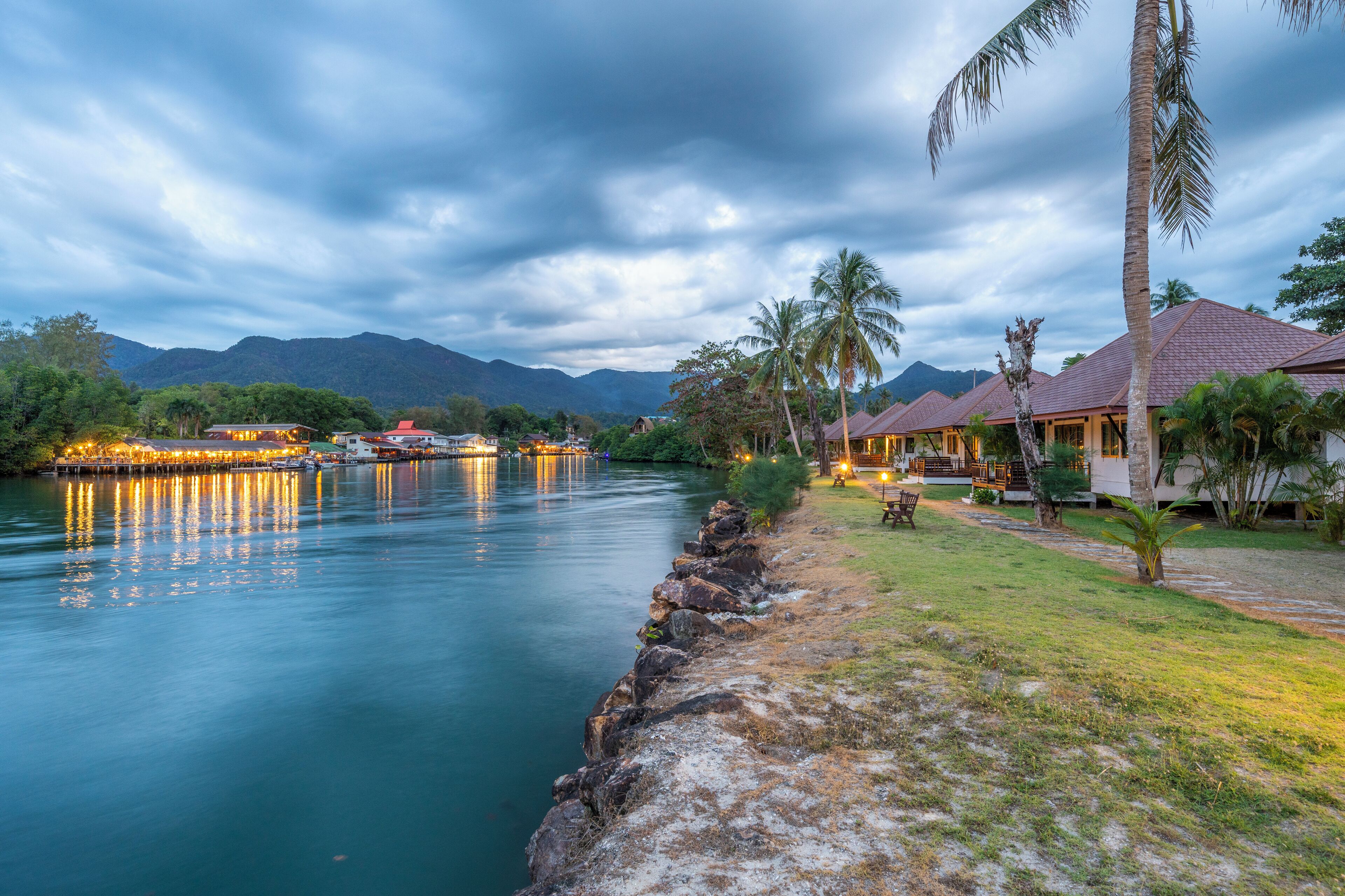 A riverside hotel with a view of mountains, a calm river, and a well-maintained lawn.