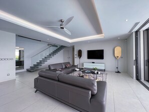 A modern living room with a grey sofa, a flat-screen TV, a ceiling fan, and a staircase.