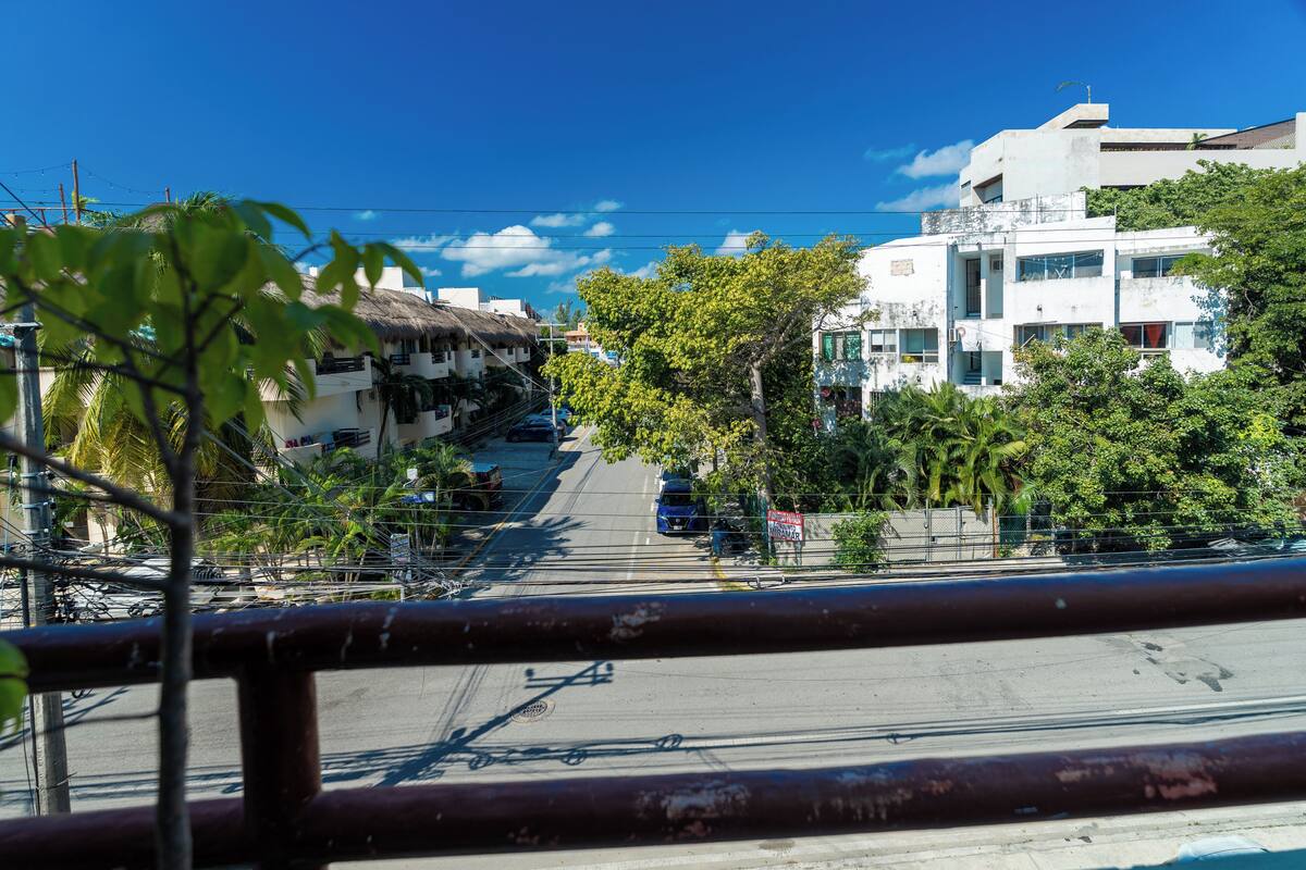 A street view with buildings, a clear sky, and a metal fence in the foreground.