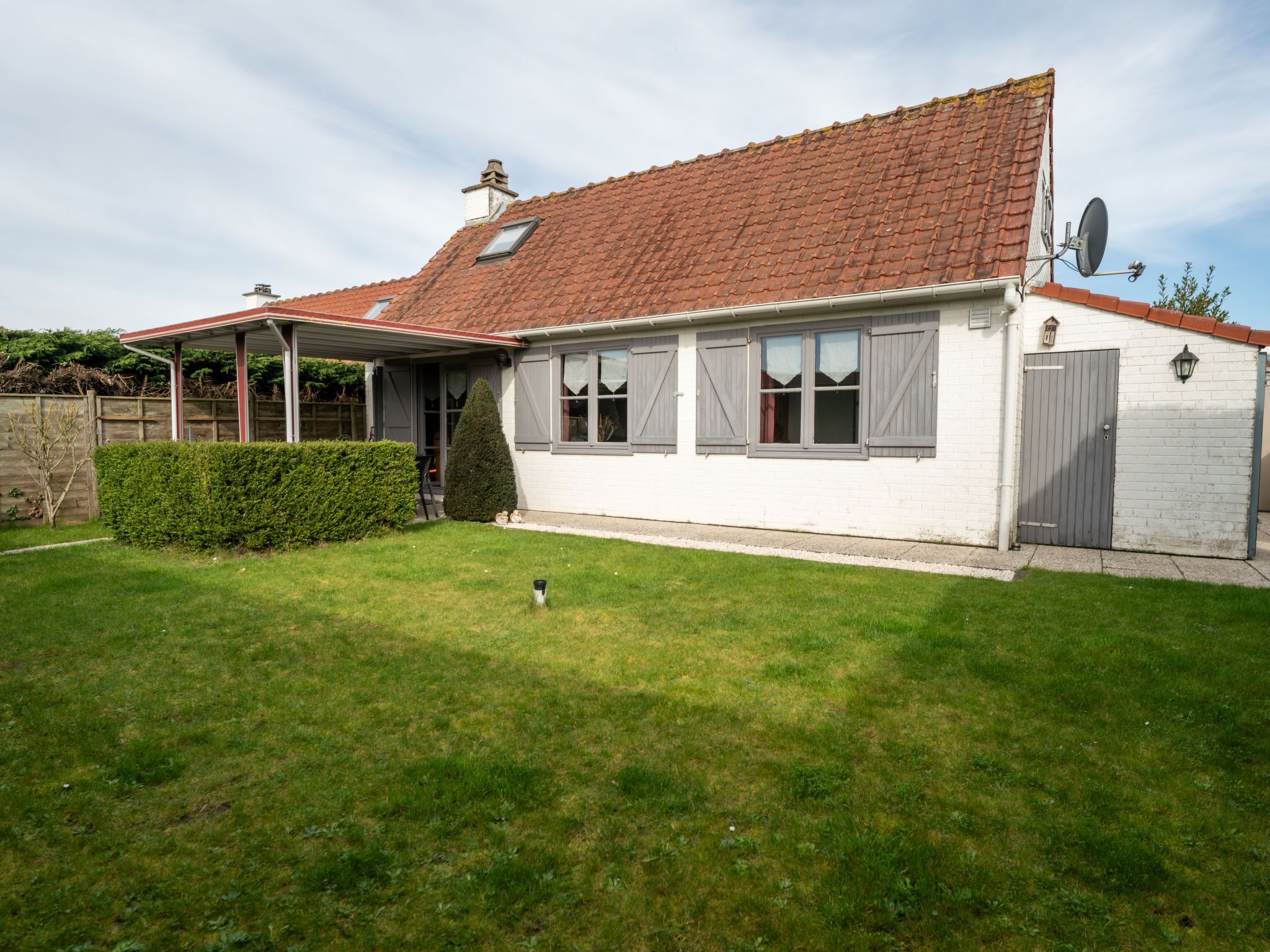 A single-story house with a red-tiled roof, white exterior walls, and a covered porch.