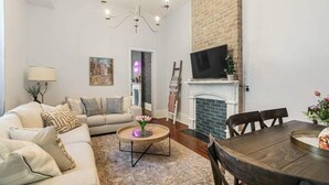 Ein Wohnzimmer mit Sofa, Couchtisch, Kamin, Fernseher und Esstisch.