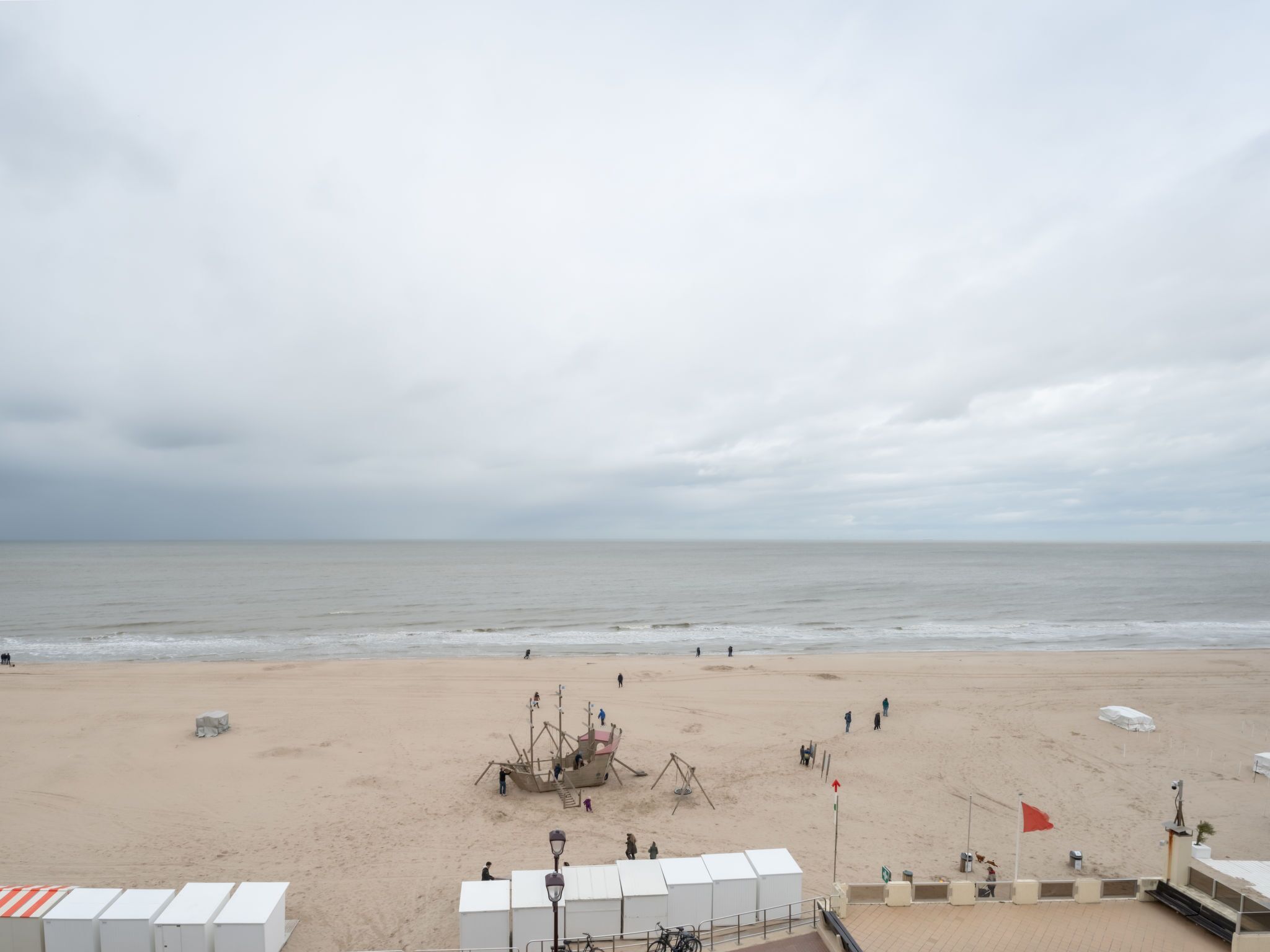 A beach with a lifeguard tower, a lifebuoy, and a flag.