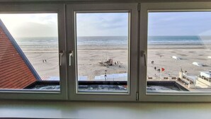 A view from a window overlooking a beach with a lifeguard tower and umbrellas. - Koekoeksnest Penthouse at the beach by Interhome (De Haan)