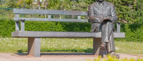 A statue of a seated man on a bench in a park.