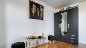 A modern room with a dark wardrobe, a small round table with a black ottoman, and a framed artwork on the wall.