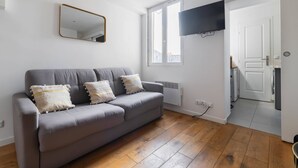A living room with a grey sofa, a mirror, and a TV mounted on the wall.