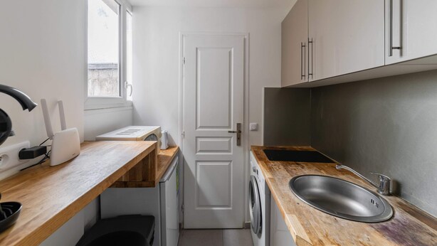 A compact kitchen with a wooden countertop, a stainless steel sink, a washing machine, and a white door.