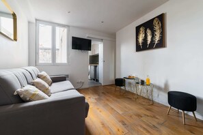 A modern living room with a grey sofa, wooden flooring, a flat-screen TV, a dining area with a small table and chairs, and a wall-mounted artwork. - Studio cosy metro saint Paul - Paris 3 - 2P (Paris)